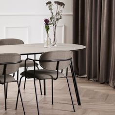 a dining table with four chairs and a vase filled with flowers on the table next to it