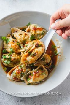 a person holding a spoon in a bowl filled with dumplings and broccoli