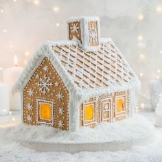 a gingerbread house with lit candles in the background and snow on the ground next to it