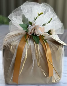 a gold gift bag with white flowers and ribbon on the top is sitting on a table