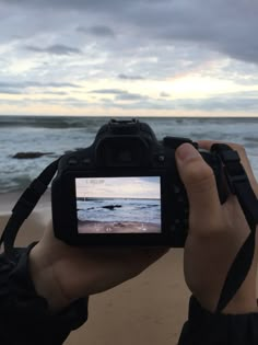 a person holding up a camera to take a photo on the beach with waves in the background