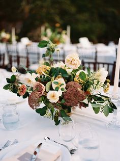 an arrangement of flowers and greenery on a table at a formal dinnereon party