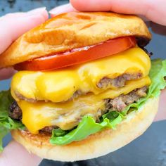 a hand holding a cheeseburger with tomato and lettuce on it's bun