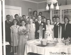 a group of people standing in front of a table with cake and candles on it