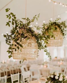 two hanging baskets filled with greenery on top of white table cloth covered tables in a tent