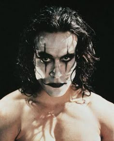 a shirtless man with his face painted white and black, standing in front of a dark background