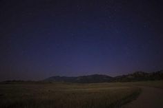 the night sky is lit up with stars above an open field and mountains in the distance