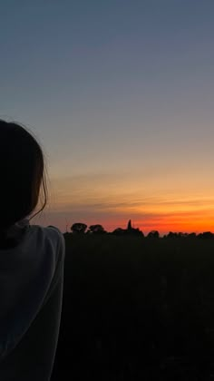 a woman standing in front of a sunset with her back to the camera and looking at something