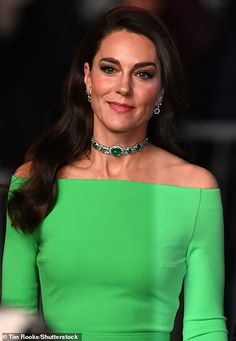 a woman in a green dress with long hair and earrings on her head, smiling at the camera