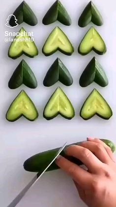 someone cutting cucumbers with a knife on a white surface and several pieces cut in half