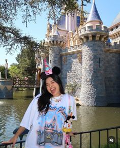 a woman standing in front of a castle wearing a minnie mouse t - shirt and holding a cupcake