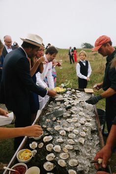 a group of people standing around a table filled with oysters and condiments