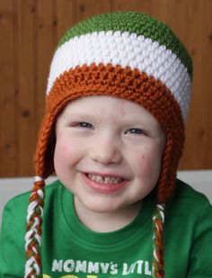 a little boy wearing a green shirt and a white and orange knitted beanie