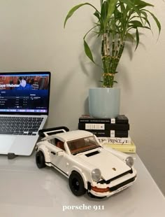 a laptop computer sitting on top of a desk next to a toy car and potted plant