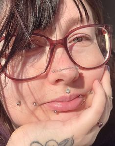 a close up of a person wearing glasses with tattoos on her face and nose piercings