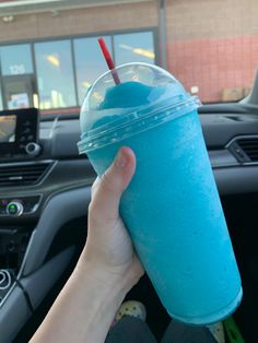 a hand holding a blue drink in front of a steering wheel with a red straw