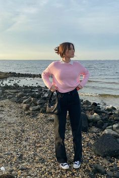 a woman standing on top of a rocky beach next to the ocean with her hands on her hips