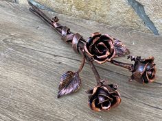 two metal roses are sitting on a wooden surface, one is broken and the other has fallen leaves