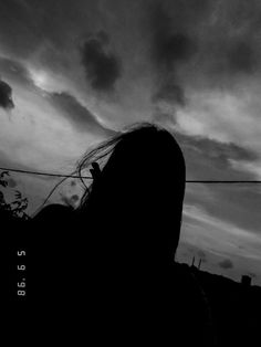 the silhouette of a woman with her hair blowing in the wind under a cloudy sky