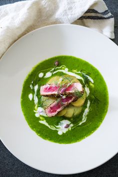 a white plate topped with green soup and sliced up radishes on top of it