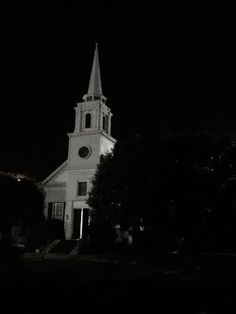 a white church with a steeple lit up at night