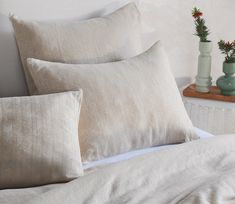 three vases with flowers are sitting on the edge of a bed next to pillows