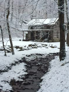 a log cabin in the woods with snow on the ground and stream running through it