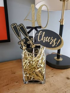 a table topped with a glass vase filled with gold foiled confetti sticks