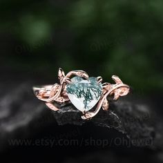 a heart shaped ring sitting on top of a piece of wood with leaves around it