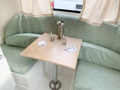 a corner table with two cups on it in front of a white couch and window