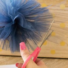 a hand holding a pair of scissors near a piece of paper with a blue tulle on it