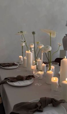 a table topped with lots of white candles next to plates and vases filled with flowers