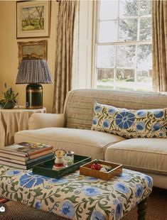 a living room with a couch, ottoman and coffee table in front of a window