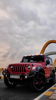 a red jeep is parked in front of a large arch with a yellow circle behind it