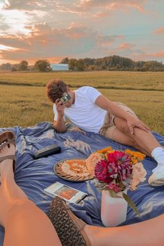 two people are laying on a blanket in the middle of an open field, one is holding a cell phone to his ear