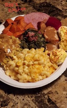 a white plate topped with macaroni and cheese covered in gravy next to meat