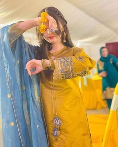 a woman in a yellow dress and blue shawl is holding her hand up to her face