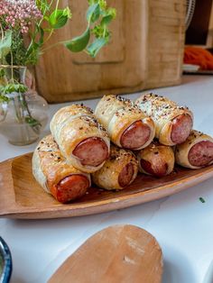 several sausages wrapped in bread on a wooden platter next to a vase with flowers