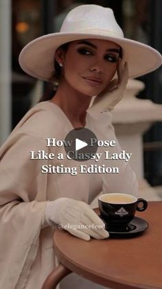 a woman sitting at a table wearing a white hat and holding a cup of coffee