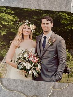 a man and woman standing next to each other in front of some trees with flowers