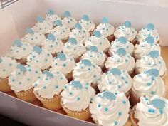 cupcakes with white frosting and blue polka dots are arranged in a box