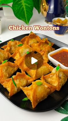 chicken wontons on a black plate with dipping sauce and green leaves in the background