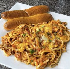 two hot dogs are on a white plate with spaghetti and meat in the foreground