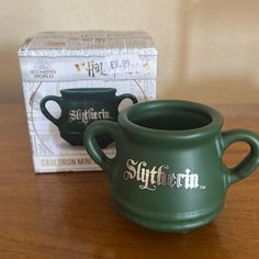 two green coffee mugs sitting on top of a wooden table next to a box