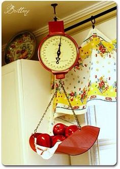 a clock hanging from the side of a kitchen wall next to some fruit on a chain