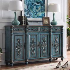 an ornately decorated sideboard with two lamps on top and a painting in the background