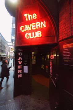 the cavern club is lit up at night with people walking past it and on the sidewalk