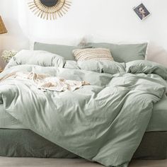 an unmade bed with green sheets and pillows in a white room next to a lamp