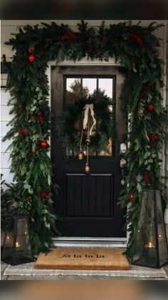 a christmas wreath on the front door of a house decorated with greenery and bells