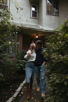 a man and woman standing in front of a house with their arms around each other